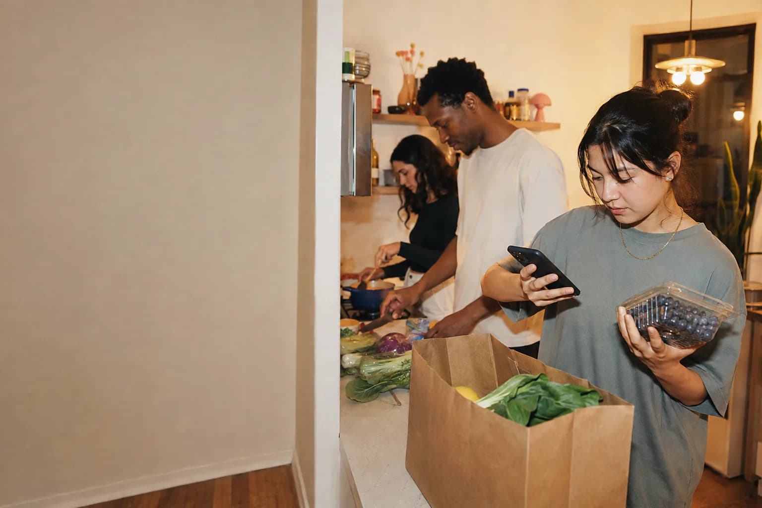 Friends preparing food while one person checks a package of blueberries with her phone